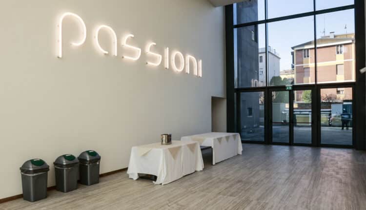 Accoglie chi entra, quasi come un monito a vivere ogni istante con slancio, la grande insegna luminosa “passioni” installata nel foyer del teatro cui dà il nome all’interno dell’ex Enel. Lo spazio, caratterizzato da grandi vetrate e da un volume per metà a tutta altezza e per metà soppalcato, consente ai frequentatori di fare una sosta prima di entrare nella sala teatrale e potrà facilmente essere luogo di incontri ed eventi. La sala del teatro, che con elementi strutturali metallici richiama la struttura industriale di un tempo, presenta una tribuna da 150 sedute apribile elettricamente in caso di spettacoli e richiudibile per consentire di utilizzare l'intero spazio su un unico livello. Sono alcune delle caratteristiche del primo stralcio dei lavori di restauro e riqualificazione dell’edificio ex Enel, all’interno del comparto dell’ex Amcm, che è giunto alle fasi finali e la parte dell’edificio rinnovata ha vissuto il suo primo momento di apertura "pubblica" in occasione del tradizionale incontro di fine anno del sindaco Gian Carlo Muzzarelli con i giornalisti modenesi promosso con l'Associazione stampa modenese, venerdì 23 dicembre. Nella porzione di edificio oggetto di lavori rimangono da completare le ultime finiture e i collaudi necessari per consegnare la struttura, che nell’arco di qualche mese potrà ospitare il primo evento di Emilia-Romagna Teatro. Intanto, con l’inizio dell’anno è prevista la presentazione del progetto relativo al secondo stralcio di lavori, finanziato con risorse del Pnrr con la collaborazione di Fondazione di Modena, attraverso il quale verrà realizzata un’altra sala teatrale e la sede unica di Ert. Rispetto alla superficie totale dello stabile di 5.500 metri, il primo stralcio di interventi, approvato dalla Soprintendenza, ha riguardato una superficie di 2.200 metri quadri, comprensiva oltre che del foyer e della sala teatrale anche dei camerini e servizi dedicati, di un bar e un ristorante al piano superiore dotato di soppalco e di un ampio terrazzo per la fruizione estiva. In particolare, lo spazio che una volta ospitava il carro ponte e i trasformatori della centrale dell’Enel ora è una sala da teatro con 150 sedute, mentre al posto delle serrande industriali di accesso all’edificio adesso ci sono ampie vetrate di ingresso e, sul “cannocchiale” di collegamento tra queste, invece dei binari su cui scorrevano i mezzi pesanti per scaricare i materiali da utilizzare nella struttura produttiva ora trova spazio il foyer, luogo dell’accoglienza del pubblico, con biglietteria e guardaroba. Sull’intero edificio è inoltre stato effettuato un intervento di adeguamento sismico e antincendio nonché opere impiantistiche esterne e un polo tecnologico in sede remota. I lavori sono realizzati dall’associazione temporanea di imprese costituita da Cme (Consorzio imprenditori edili di Modena) e Ot srl di Mirandola (l’impresa esecutrice è Sacogen srl) per un valore complessivo pari a circa 7 milioni 600 mila euro, frutto di adeguamenti e ulteriori interventi resisi necessari in corso d’opera, del riconoscimento dei maggiori costi delle materie prime e dell’energia elettrica e di atti di transazione con l’azienda legati a miglioramenti progettuali. Per l’intervento, il Comune ha ottenuto un finanziamento europeo di due milioni e 850 mila euro sull’Asse 5 (Valorizzazione delle risorse artistiche, culturali e ambientali) del Por Fesr Emilia-Romagna 2014-2020 cui ha aggiunto risorse proprie fino a copertura del costo complessivo. Nel comparto dell’ex Amcm, il Comune ha già realizzato autonomamente, grazie anche alle risorse europee, il recupero e la riqualificazione dell'edificio ex Aem, oggi Laboratorio aperto, ed è attualmente in corso l’intervento di rigenerazione urbana pubblico-privata del comparto che consegnerà ai modenesi il Parco della Creatività, con una nuova palestra, una piazza con funzioni di arena, parcheggi interrati e una galleria commerciale oltre a edifici residenziali